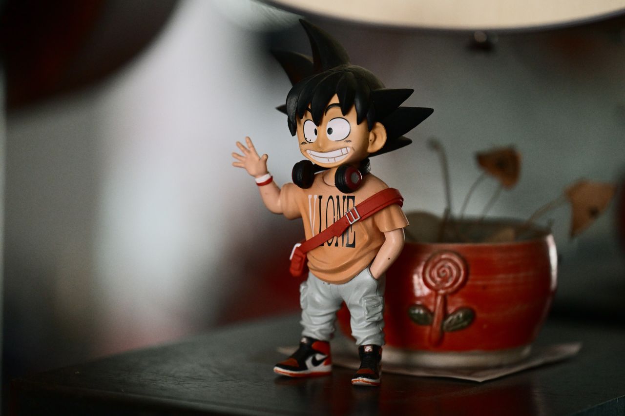 Anime figurine with headphones, standing on a desk beside a colorful pot, indoors.